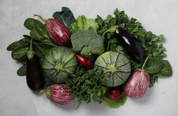 Assortment of fresh vegetables and herbs such as zucchini, eggplant, onion, broccoli, arugula, spinach and cilantro on light gray background. Vegetarian food. View from above