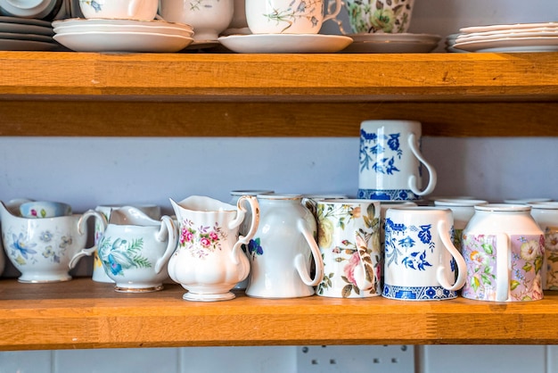 Photo assortment of hand painted ceramic floral pattern teacups with mugs on shelves