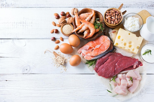 Assortment of healthy protein source and body building food Meat beef salmon shrimp chicken eggs dairy products milk cheese yogurt beans quinoa nuts oat meal Copy space background top view