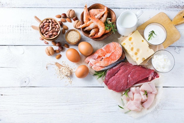 Assortment of healthy protein source and body building food Meat beef salmon shrimp chicken eggs dairy products milk cheese yogurt beans quinoa nuts oat meal Copy space background top view