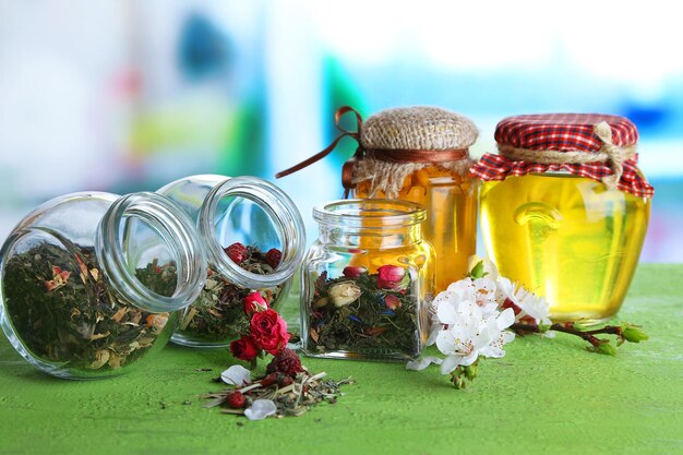 Assortment of herbs and tea in glass jars on wooden table on bright background