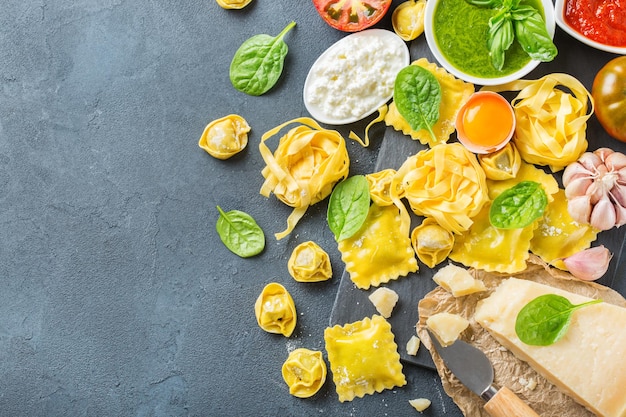 Assortment of italian food and ingredients ravioli with ricotta and spinach pasta tortellini pesto tomato sauce olive oil parmesan cheese Copy space background top view flat lay