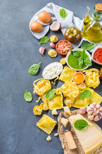 Assortment of italian food and ingredients ravioli with ricotta and spinach pasta tortellini pesto tomato sauce olive oil parmesan cheese Copy space background top view flat lay