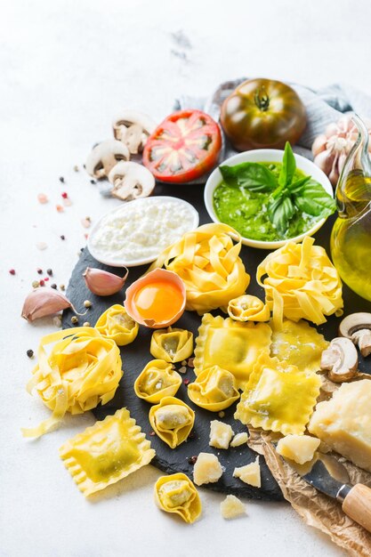 Assortment of italian food and ingredients ravioli with ricotta and spinach pasta tortellini pesto tomato sauce olive oil parmesan cheese Copy space background
