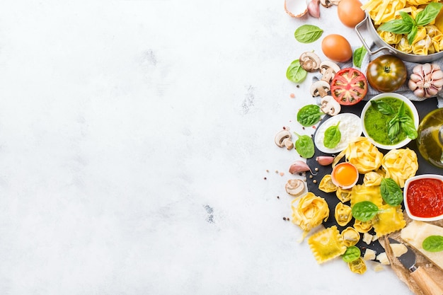 Assortment of italian food and ingredients ravioli with ricotta and spinach pasta tortellini pesto tomato sauce olive oil parmesan cheese Top view flat lay copy space background