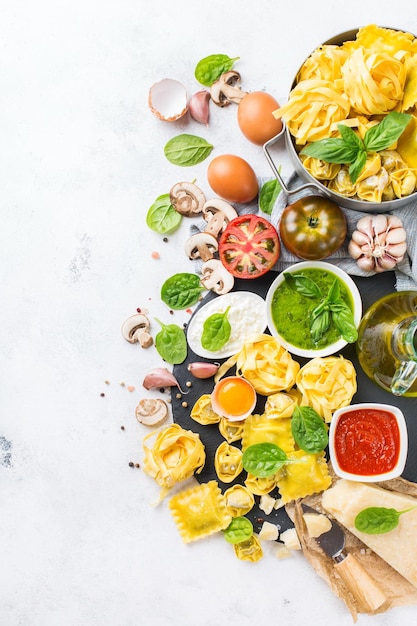 Assortimento di cibo italiano e ingredienti ravioli con ricotta e spinaci pasta tortellini pesto salsa di pomodoro olio d'oliva parmigiano vista dall'alto piatto laico copia spazio sfondo