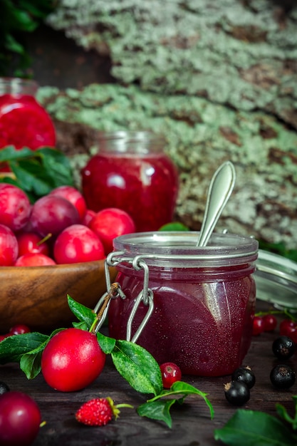 Photo assortment of jam in glass jars,  fresh berries and fruit plum