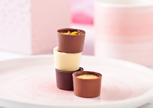 컵과 선물 상자가있는 분홍색 접시에 다양한 고급 흰색과 어두운 초콜릿 사탕 종류