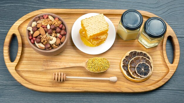 Assortment of nuts and assorted dried citrus fruits and fresh floral honeycomb honey and pollen on kitchen wooden board. useful vitamin food for the human body