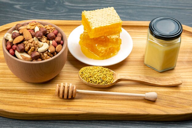 Assortment of nuts and assorted dried citrus fruits and fresh floral honeycomb honey and pollen on kitchen wooden board useful vitamin food for the human body