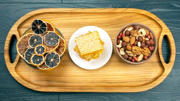 Assortment of nuts and assorted dried citrus fruits and fresh floral honeycomb honey and pollen on kitchen wooden board useful vitamin food for the human body