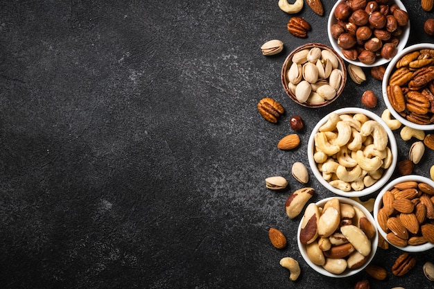 Photo assortment of nuts in the bowls cashew hazelnuts pecan almonds brazilian nuts and pistachios at light stone table top view with copy space