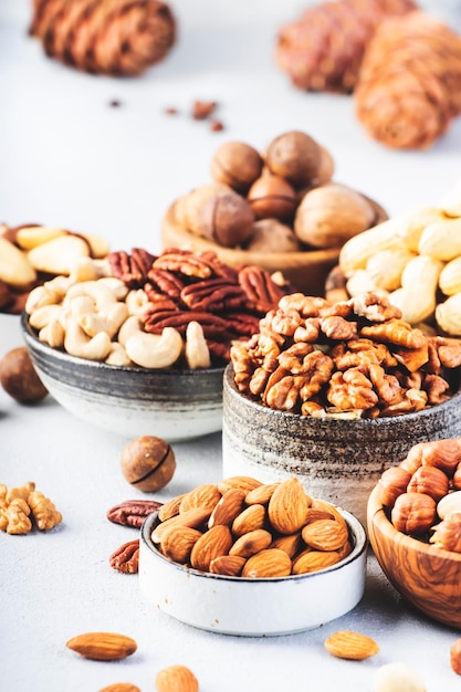 Assortment of nuts in bowls Cashews hazelnuts walnuts pistachios pecans pine nuts peanuts macadamia almonds brazil nuts Food mix on gray background copy space