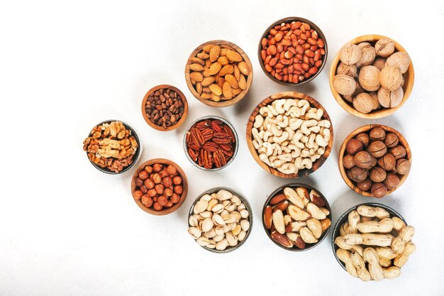 Assortment of nuts in bowls Cashews hazelnuts walnuts pistachios pecans pine nuts peanuts macadamia almonds brazil nuts Food mix on white background top view copy space