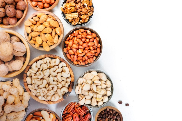 Assortment of nuts in bowls Cashews hazelnuts walnuts pistachios pecans pine nuts peanuts macadamia almonds brazil nuts Food mix on white background top view copy space