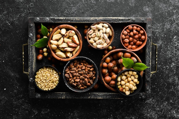 Assortment of nuts pistachios hazelnuts pine nuts on a black stone background free space for your text Top view