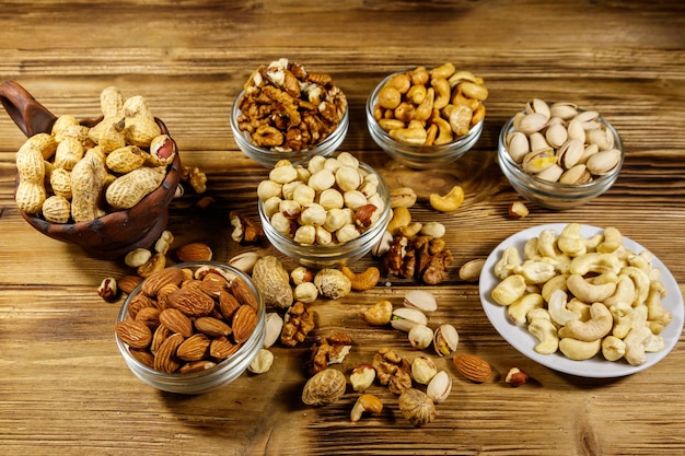 Assortment of nuts on wooden table Almond hazelnut pistachio peanut walnut and cashew in small bowls Healthy eating concept