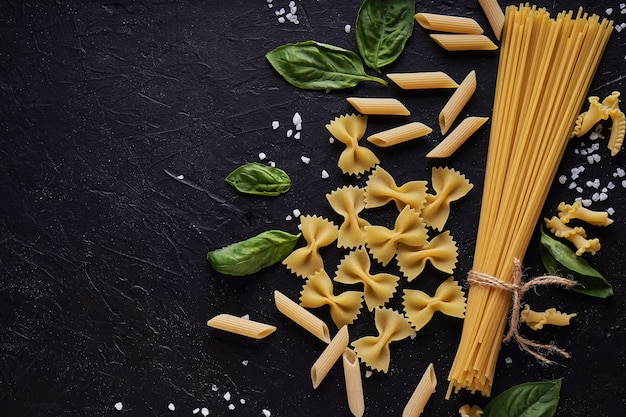 Assortment of pasta with green leaf on dark stone background