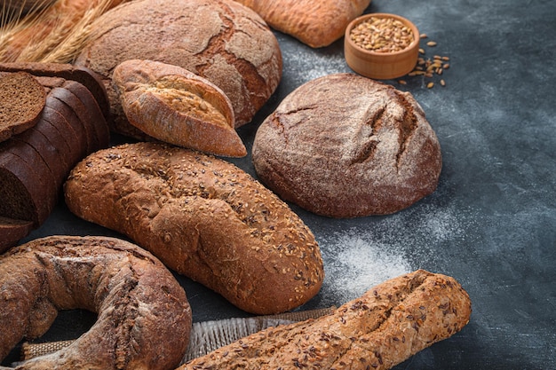 Assortment of rye and wheat bread on a dark background with flour. Side view, copy space.