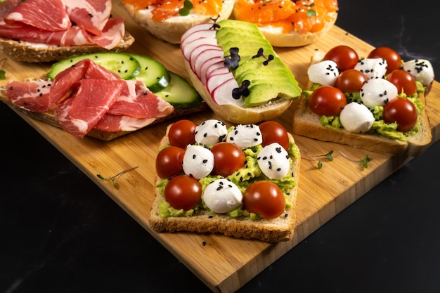 An assortment of sandwiches with fish, cheese, meat and vegetables lay on the board and a bun