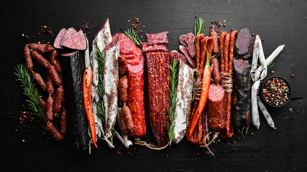 Assortment of sausages salami and fuet Dried and smoked salami on black wooden background Top view