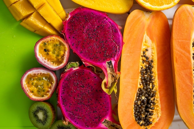 Assortment of sliced tropical exotic fruits on white tray. Top view. Close up. Healthy vegan breakfast of raw papaya, orange, mango, dragon fruit, kiwi, maracuja. Summer, food concept.