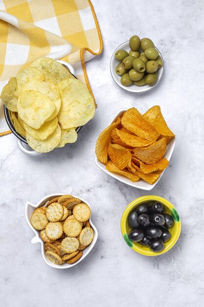 Assortimento di snack a casa con patatine fritte, birra, cracker, olive verdi e nere sul tavolo di marmo