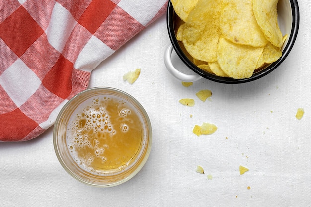 Photo assortment of snacks at home with potato chips, beer, crackers, green and black olives on table with white linen tablecloth