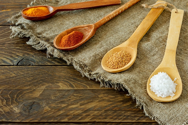 Assortment of spices in wooden spoons on a burlap on wooden background.