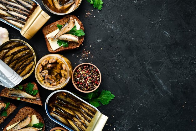 Assortment of sprats in oil Smoked fish On a black background top view Free copy space