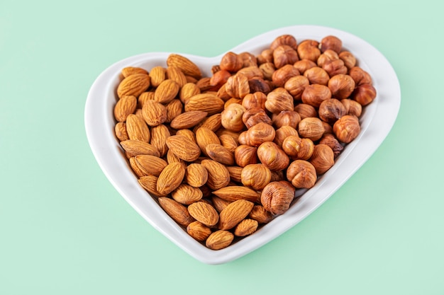 Assortment of various types of nuts in a heart shaped bowl on mint background