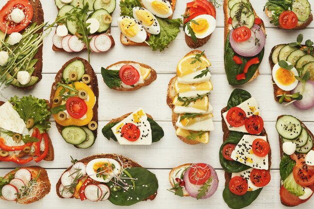 Assortment of vegetarian wholegrain sandwiches on white rustic wood, top view. Vegan party food table with organic vegetable bruschettas. Healthy lifestyle and eating right concept