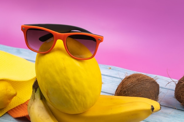 An assortment of yellow fruits and glasses lies on a pink background