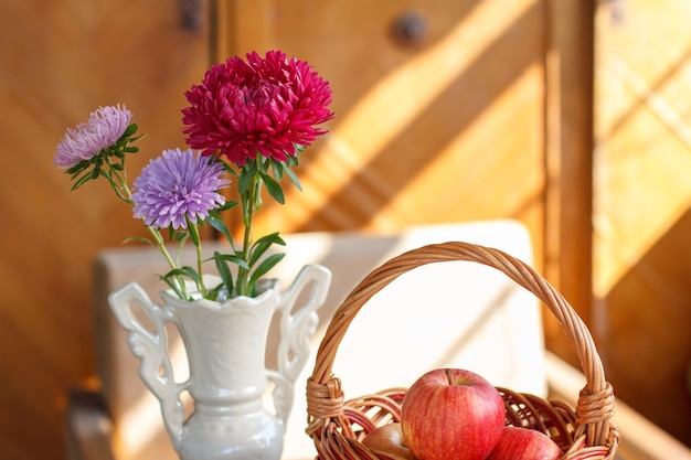 Aster flowers in vase wicker basket with red apples on a porch in a country house