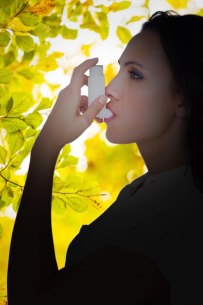 Asthmatic brunette using her inhaler against detail shot of leaves