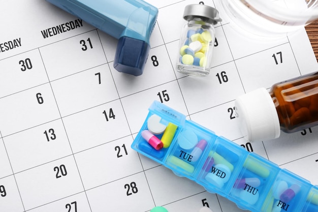 Foto astma inhalator en verschillende pillen op een papieren kalender