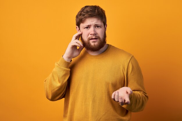 Astonished attractive male has ginger long beard, wonders sudden news, keeps mouth slightly opened, stares at camera, wears casual clothes and spectacles, poses against white wall with blank space