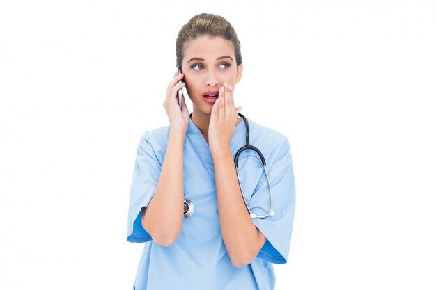 Astonished brown haired nurse in blue scrubs making a phone call