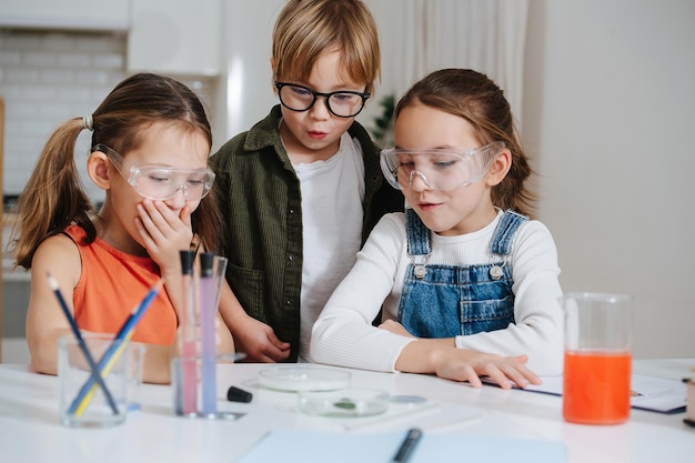 Astonished little kids doing home science project, looking at the glass dish