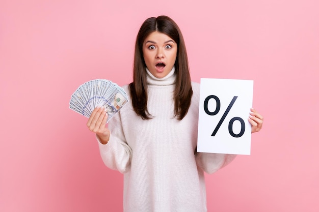 Astonished shocked brunette female holding paper with percent mark and dollar banknotes bank offer