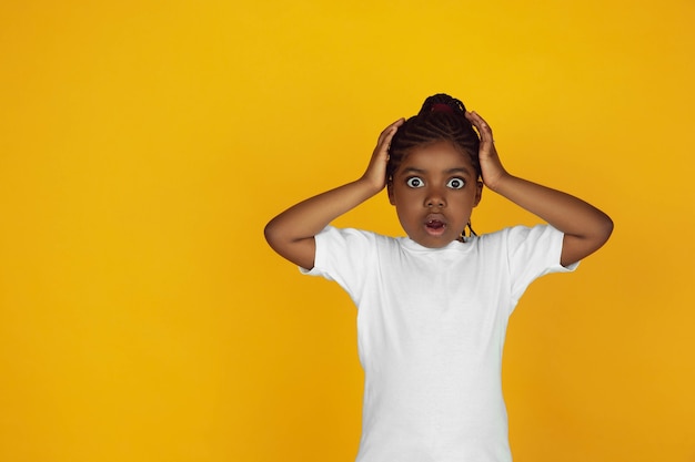Удивлен, потрясен. Портрет маленькой афро-американской девушки, изолированные на желтом фоне студии. Красиво, весело. Понятие человеческих эмоций, выражения лица, продаж, рекламы. Copyspace. Выглядит мило.