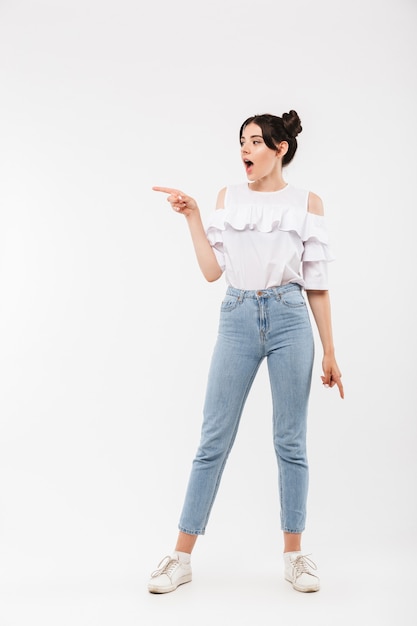 astonished woman with double buns hairstyle pointing finger aside at copyspace, isolated on white