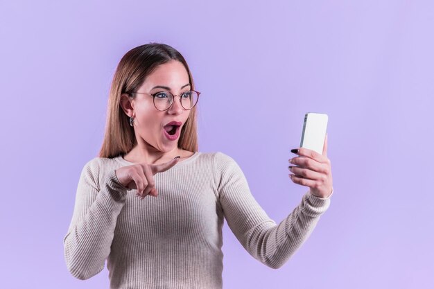 Astonished woman with glasses pointing at her phone