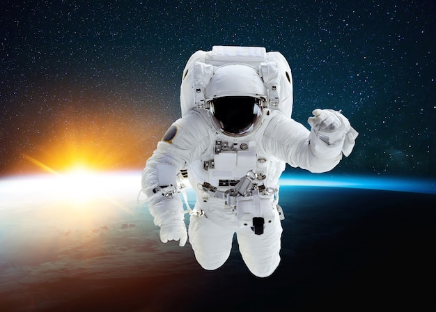 素晴らしい夕日と星と青い惑星地球の背景に宇宙を飛んでいる宇宙飛行士。ミッションの宇宙人と宇宙空間に浮揚