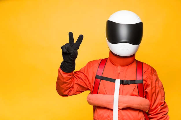 Astronaut with orange spacesuit making a victory gesture on yellow background