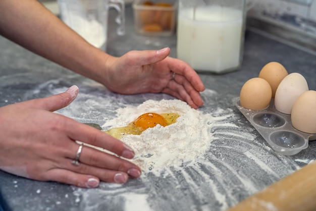 Фото За столом женщина готовит ужин, разбивает яйца и месит тесто для запеканки.