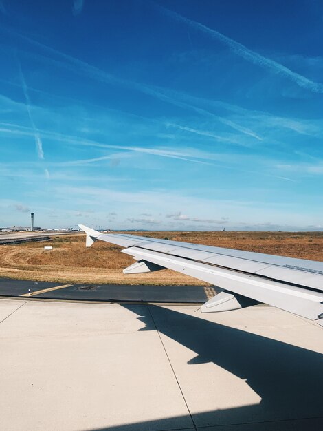 Фото В аэропорту на взлетно-посадочной полосе готовый отправиться на солнечный день крыло самолета и голубое небо
