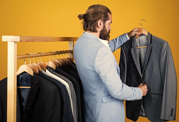 Atelier or wardrobe true gentleman with groomed hair male beauty and fashion showroom concept bearded man in formalwear elegant businessman choose elegant apparel for formal event Cool and sexy