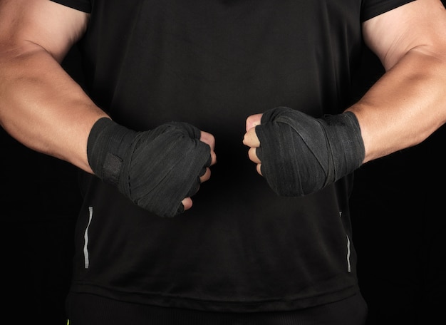 Athlete in black uniform is standing in a rack with strained muscles, his hands are wrapped in a black textile bandage