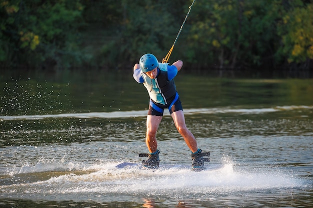 An athlete does a trick on the water A rider jumps on a wakeboard against a background of a green forest Sunset on the lake